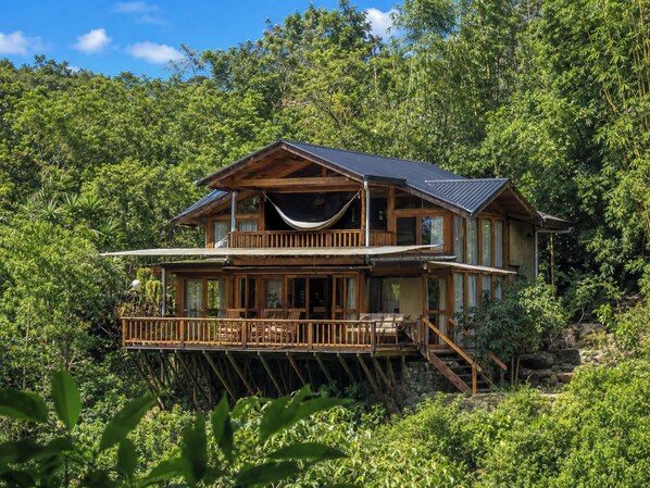 Eine zweistöckige Holzhütte mit Balkon, umgeben von dichtem Wald.