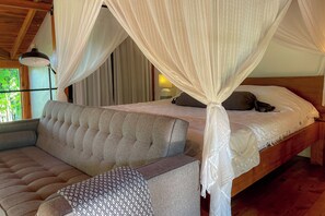 A bedroom with a canopy bed, a sofa, and a patterned ottoman.