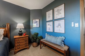 A bedroom with a bed, a nightstand with a lamp, a dresser, a bench, and wall-mounted artwork. - Ridgeview Lodge at Beaver Lake (Garfield)