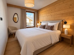 A bedroom with a large bed, a chair, a bedside table with a lamp, a mirror, and a window with curtains. - 10m from ski slopes, 3rd floor, fitness, swimming pool, sauna, hammam, terrace, parking, tv (Huez)