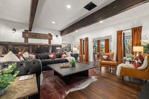 Uma sala de estar ampla com um sofá preto grande, uma mesa de centro de madeira e uma poltrona de couro marrom.