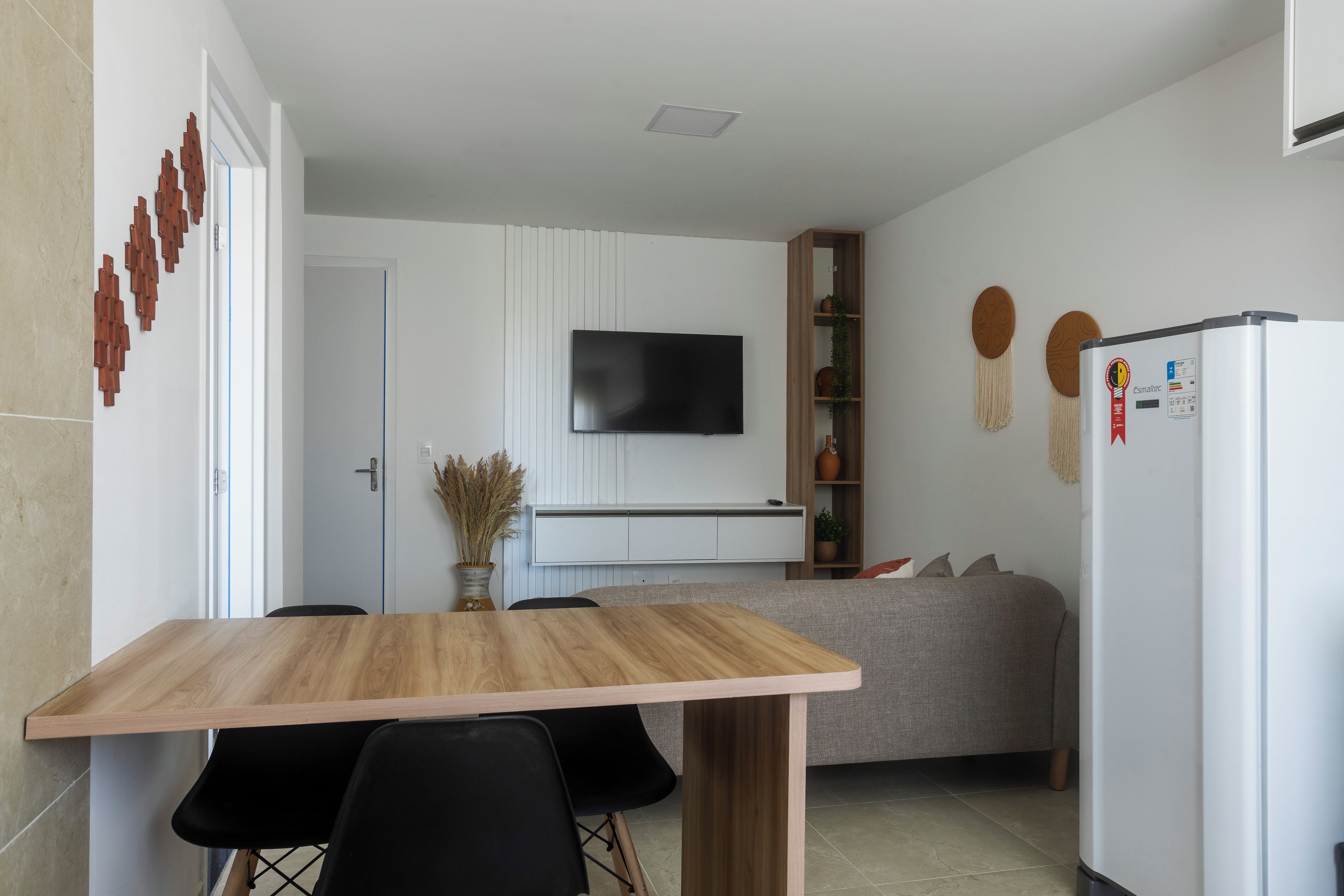 Una cocina moderna con una mesa de madera, sillas negras, un televisor integrado y un refrigerador blanco.