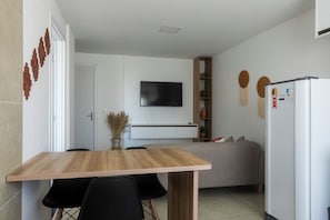 A modern kitchen with a wooden table, black chairs, a built-in TV, and a white refrigerator. - Lzt Confort (Caruaru)