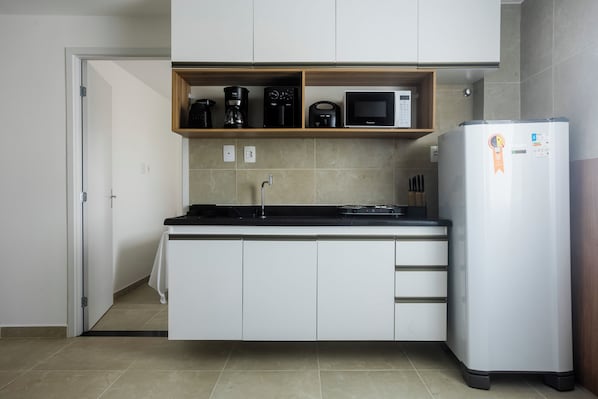 A compact kitchen with white cabinets, a built-in microwave, a coffee maker, and a refrigerator. - Lzt Confort (Caruaru)