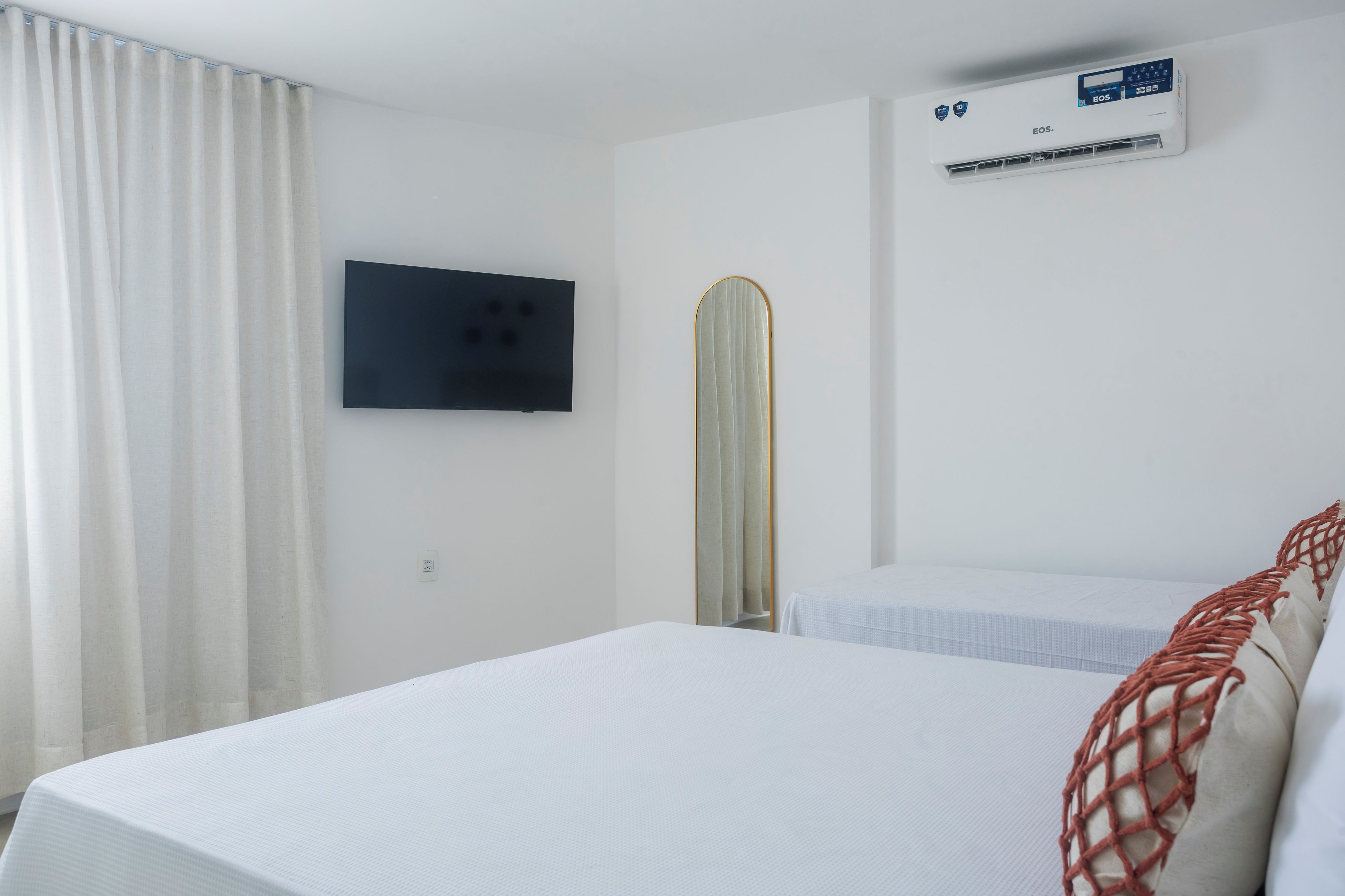 A hotel room with a bed, a television mounted on the wall, and an air conditioning unit.
