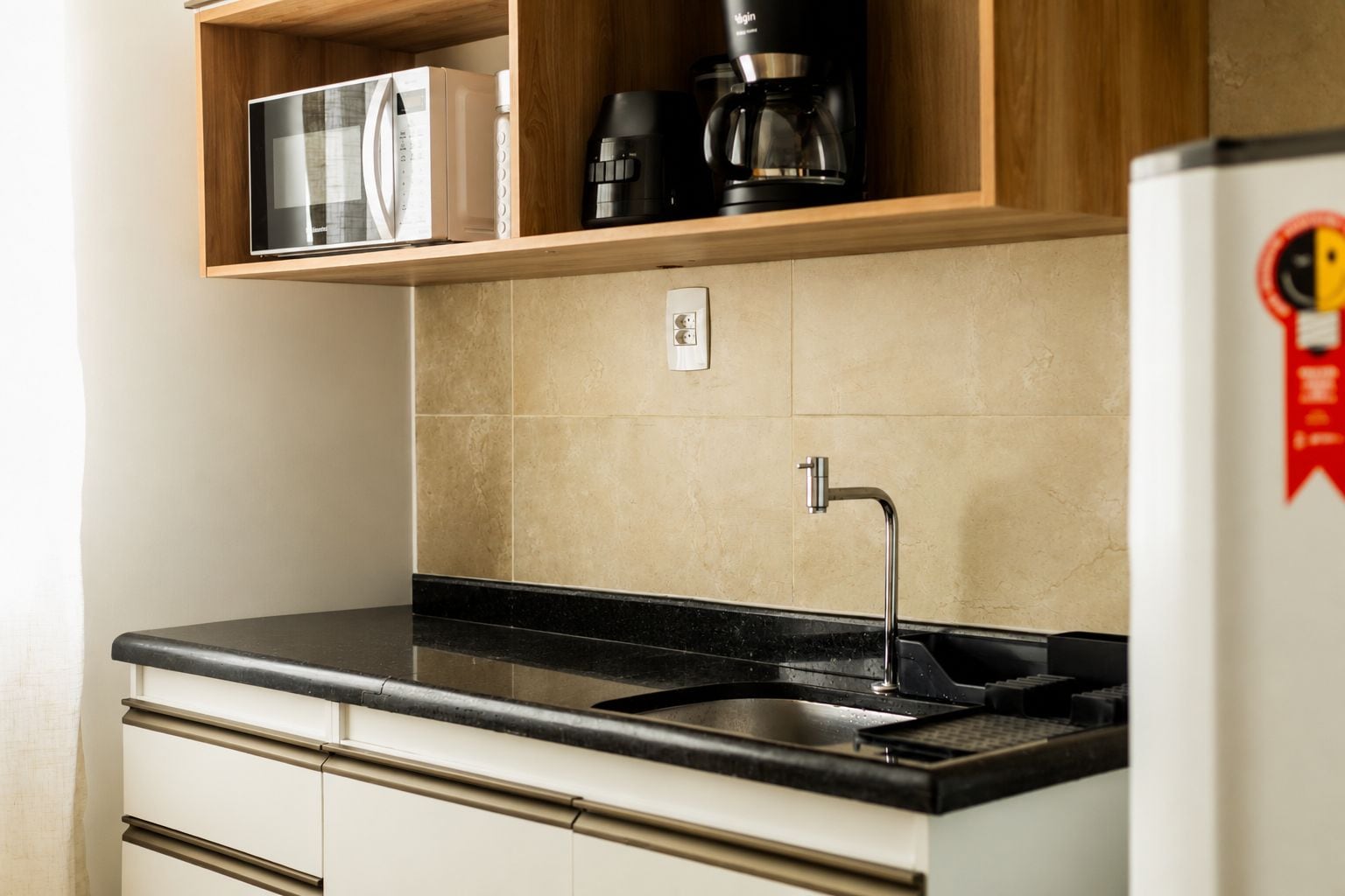 A kitchen with a black countertop, a stainless steel sink, and a wooden shelf above.