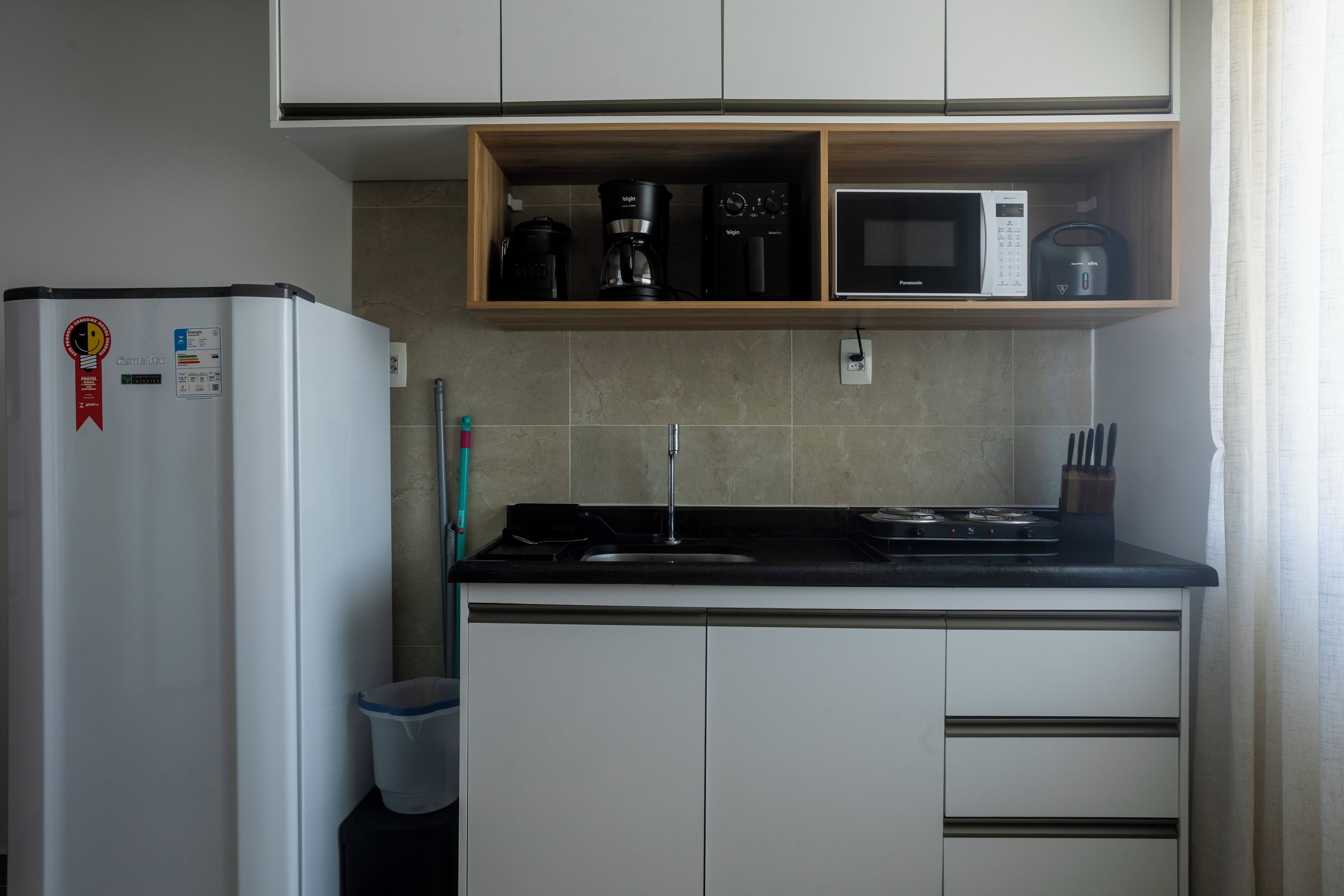 A compact kitchen with a refrigerator, microwave, coffee maker, and a small sink.