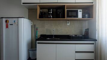 A compact kitchen with a refrigerator, microwave, coffee maker, and a small sink.