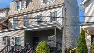A multi-story residential building with a front porch, a staircase, and a small garden area.