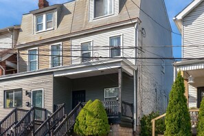 A multi-story residential building with a front porch, a staircase, and a small garden area. - Summit Row | Porch House (Pittsburgh)