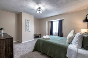 A hotel room with a bed, a desk, a chair, a small table, a potted plant, and a ceiling light fixture. - Summit Row | Porch House (Pittsburgh)