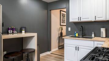 A modern kitchen with white cabinets, a black faucet, and a gas stove. There are two stools and a small table with kitchen items.