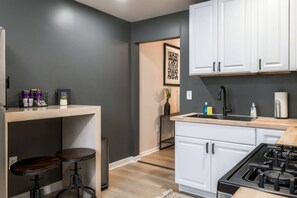 A modern kitchen with white cabinets, a black faucet, and a gas stove. There are two stools and a small table with kitchen items. - Summit Row | Porch House (Pittsburgh)