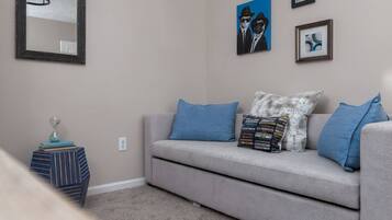 A living room with a grey sofa, blue cushions, a small side table with books, and a mirror on the wall.