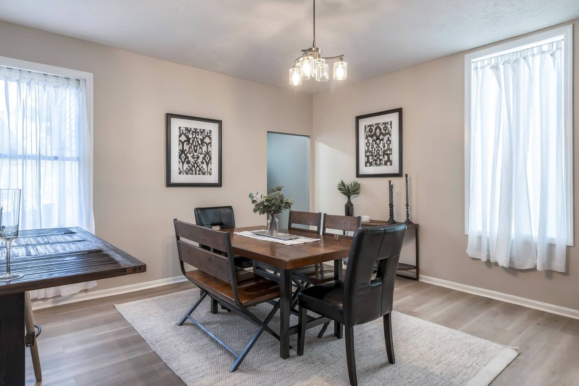 A dining area with a wooden table, black chairs, a chandelier, and framed artwork on the walls.