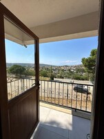 Un balcón con vistas a un paisaje urbano, una barandilla de metal y una puerta que da al balcón.