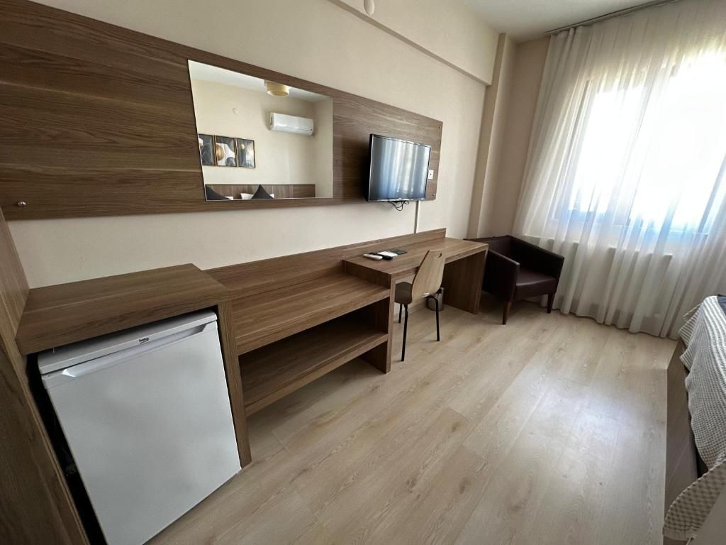 A hotel room with a wooden desk, a television, a small refrigerator, and a large window with curtains.