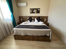 Habitación de hotel con cama, cabecera, aire acondicionado de pared y mesita de noche con lámpara.