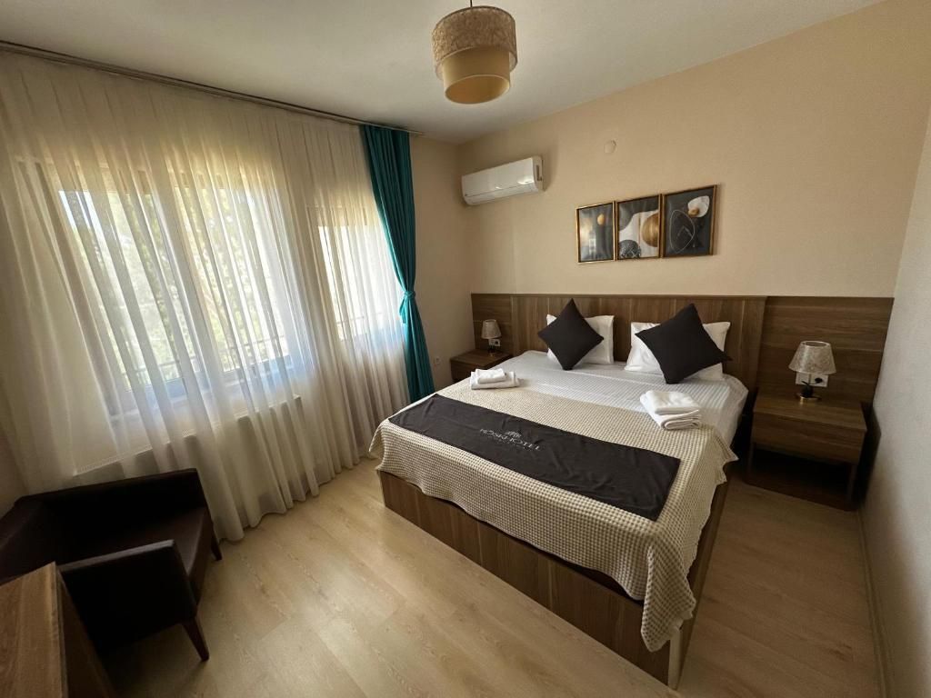 Una habitación de hotel con una cama grande, una mesita de noche, una lámpara y un ventanal con cortinas.