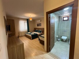 Habitación de hotel con cama, escritorio, silla, mesita, espejo y baño con inodoro y lavamanos.