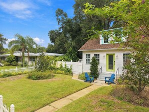 A residential property with a well-maintained lawn, a white picket fence, and a house with a green door. - Hot Tub - Walk Downtown SH - 4BR (Safety Harbor)