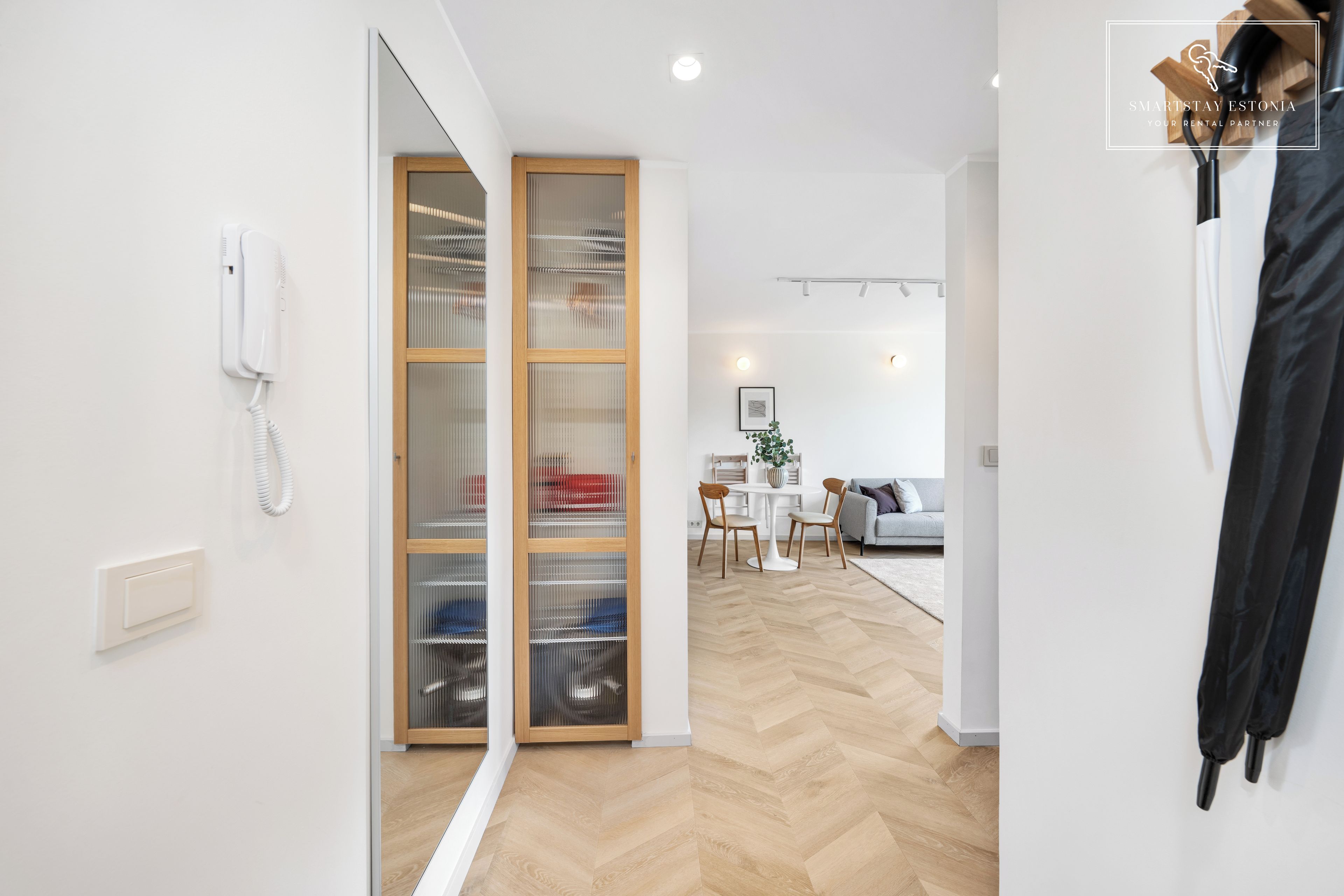 Un interior moderno con suelo de madera, un teléfono blanco montado en la pared y una puerta corredera de cristal que da a un comedor.