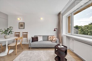 Ein modernes Wohnzimmer mit einem grauen Sofa, Holzstühlen, einem kleinen Tisch und Blick ins Grüne.