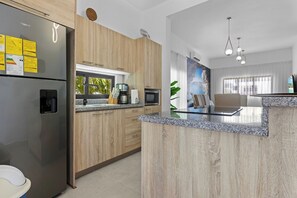 A modern kitchen with a stainless steel refrigerator, wooden cabinets, a granite countertop, and a large island. - 2BR Townhome w/Fast Wi-Fi, Backyard, Gazebo & Pool (Punta Cana)