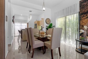 A modern dining area with a glass-top table, beige upholstered chairs, and a large window with sheer curtains. - 2BR Townhome w/Fast Wi-Fi, Backyard, Gazebo & Pool (Punta Cana)