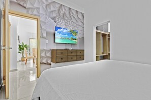 A bedroom with a bed, a TV mounted on the wall, a wooden dresser, and a geometric wall design. - 2BR Townhome w/Fast Wi-Fi, Backyard, Gazebo & Pool (Punta Cana)