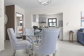 A modern living room with a glass dining table, two upholstered chairs, a sofa, and a kitchen in the background. - 3BR Villa w/ Patio, Pool Near Downtown & Beaches (Punta Cana)