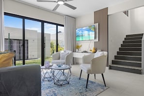 A modern living room with a flat-screen TV, a dining area, and a staircase. - 3BR Villa w/ Patio, Pool Near Downtown & Beaches (Punta Cana)