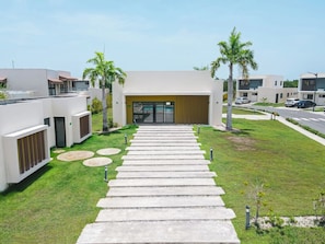 A modern building with a central entrance, surrounded by a well-maintained lawn and palm trees. - 3BR Villa w/ Patio, Pool Near Downtown & Beaches (Punta Cana)