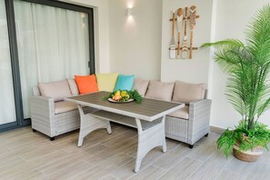 A wicker sofa with colorful cushions, a wooden table with fruit and greenery, and a potted plant. - High-end 2BR w/Private Pool + BBQ + Steps to Beach (Punta Cana)