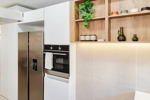 A modern kitchen with a stainless steel refrigerator, oven, and built-in shelves with decorative items. - High-end 2BR w/Private Pool + BBQ + Steps to Beach (Punta Cana)