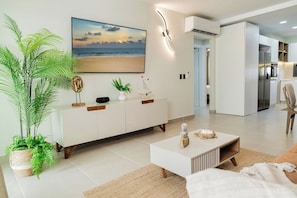 A modern living room with a large beach view painting, a white console table, and a potted plant. - High-end 2BR w/Private Pool + BBQ + Steps to Beach (Punta Cana)