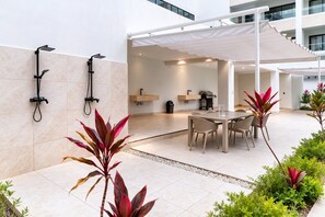 A modern outdoor patio with a dining area, two showers, and a covered seating area. - High-end 2BR w/Private Pool + BBQ + Steps to Beach (Punta Cana)