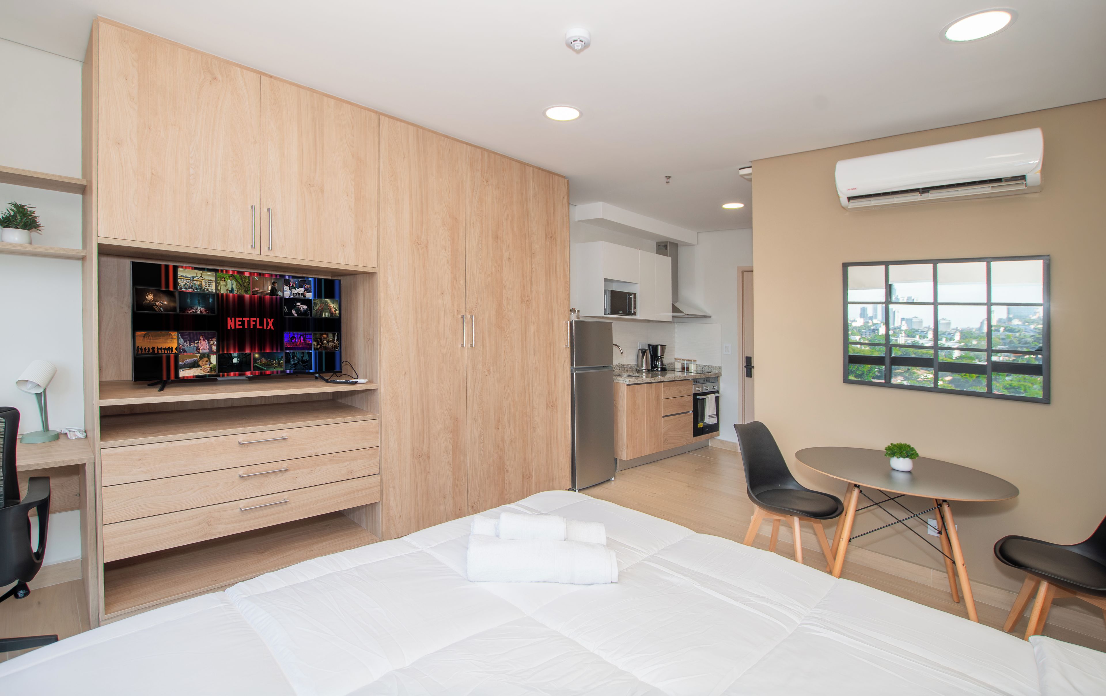 A modern bedroom with a bed, a TV with a Netflix shelf, a kitchenette, and a dining area with a view.