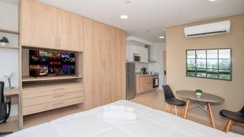 A modern bedroom with a bed, a TV with a Netflix shelf, a kitchenette, and a dining area with a view.