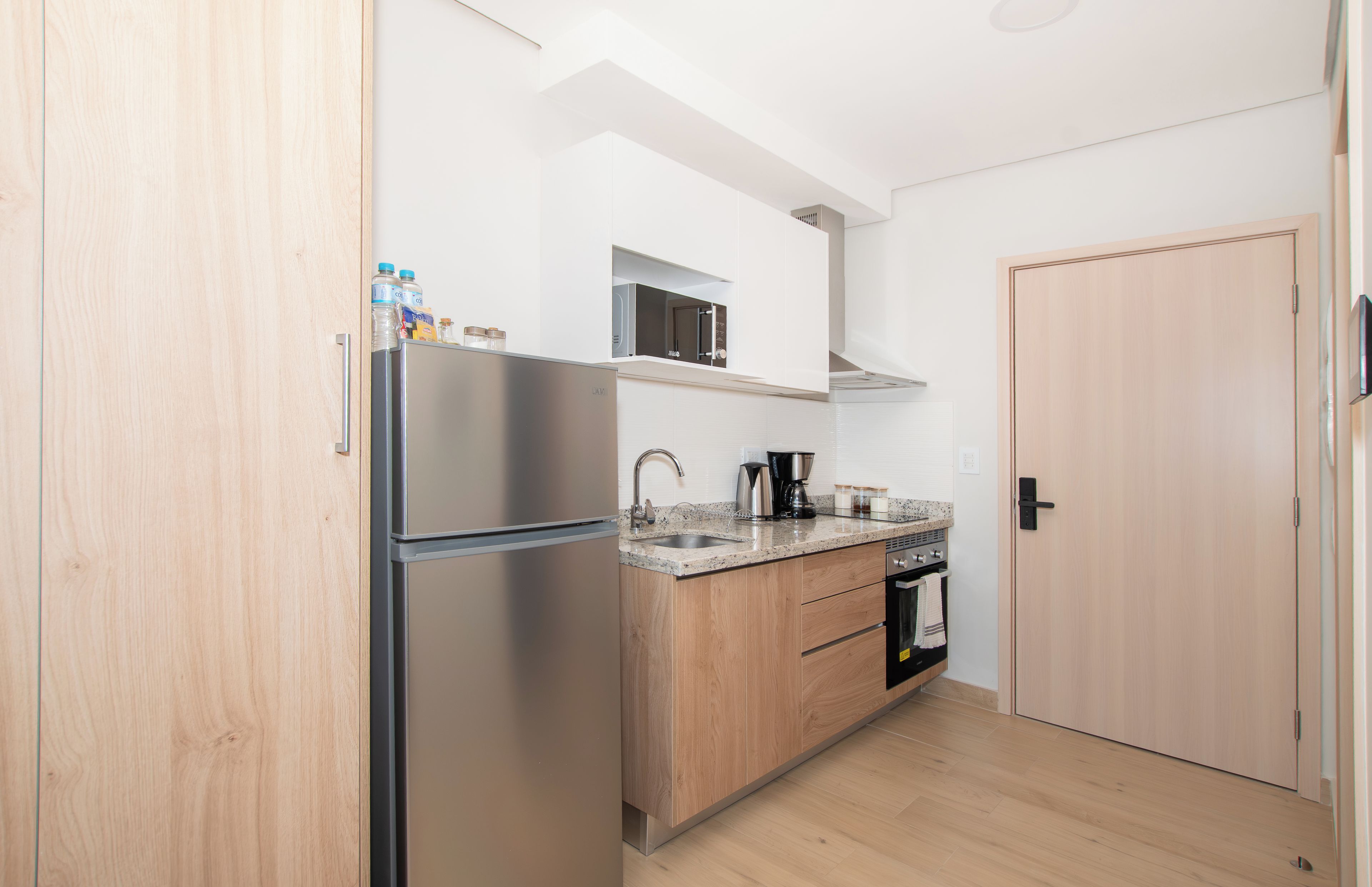 Een moderne keuken met een roestvrijstalen koelkast, een magnetron, een koffiezetapparaat en houten kastjes.