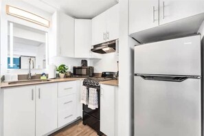A modern kitchen with white cabinets, a stainless steel refrigerator, a microwave, and a stove. - Near Disney + Pool + Gym + Park | Orl (Kissimmee)