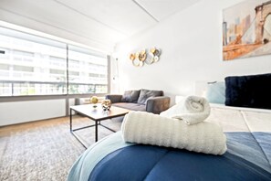 A modern living room with a sofa, a coffee table, and a window with a view of buildings. - Near Disney + Pool + Gym + Park | Orl (Kissimmee)