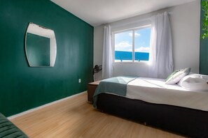 A bedroom with a bed, a window with curtains, a bedside table, and a mirror on the wall. - Apto c Churrasqueira e Garagem - Jardim Iate Clube (Balneário Camboriú)