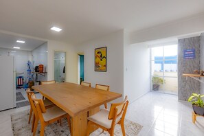 A conference room with a wooden table and chairs, a painting on the wall, and a view through a glass door. - Apto c Churrasqueira e Garagem - Jardim Iate Clube (Balneário Camboriú)