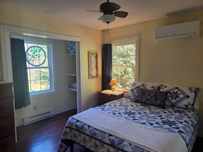 Un dormitorio con cama, mesita de noche, ventana con cortinas, ventilador de techo y aire acondicionado instalado en la pared.