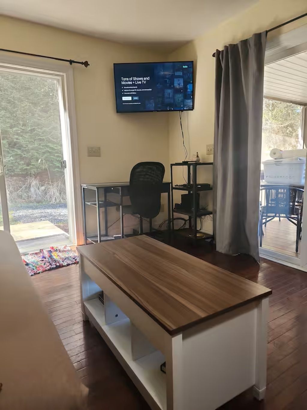 A room with a wooden table, a TV mounted on the wall, a chair, and a sliding glass door leading to an outdoor area.