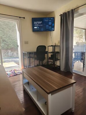 A room with a wooden table, a TV mounted on the wall, a chair, and a sliding glass door leading to an outdoor area.