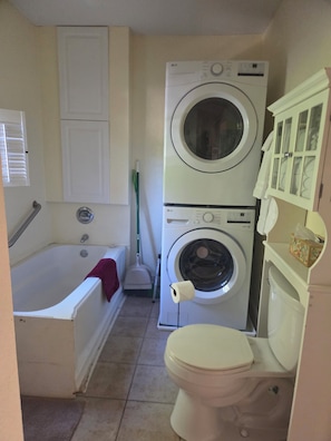 A compact bathroom with a white bathtub, a toilet, and stacked laundry machines. - Peaceful cottage in a private setting on 12 acres in the country (Weaverville)