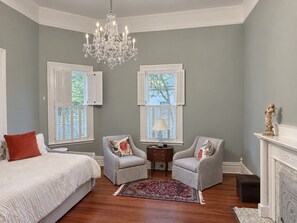A bedroom with a large bed, two armchairs, a chandelier, and a fireplace. - Restored Historic Home with Southern Porch Charm / Walk to Downtown Eufaula (Eufaula)
