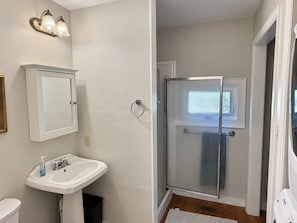 A bathroom with a white sink, a glass shower enclosure, and a white door. - Restored Historic Home with Southern Porch Charm / Walk to Downtown Eufaula (Eufaula)